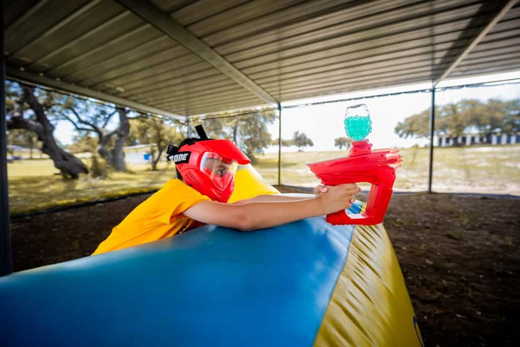 A child wearing a red helmet playing paintball in an outdoor covered area.