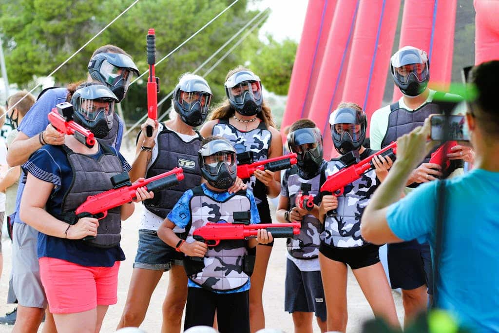 A group of people in protective gear posing for a photo during a paintball game outdoors.