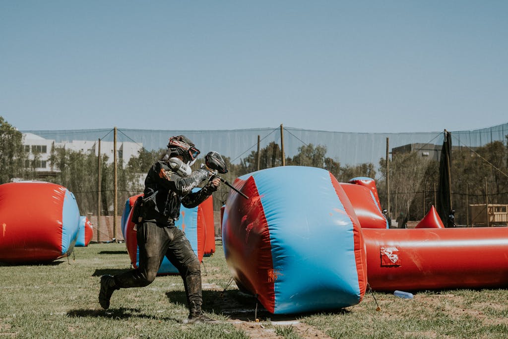 A player in action during an intense paintball game on a sunny outdoor field.