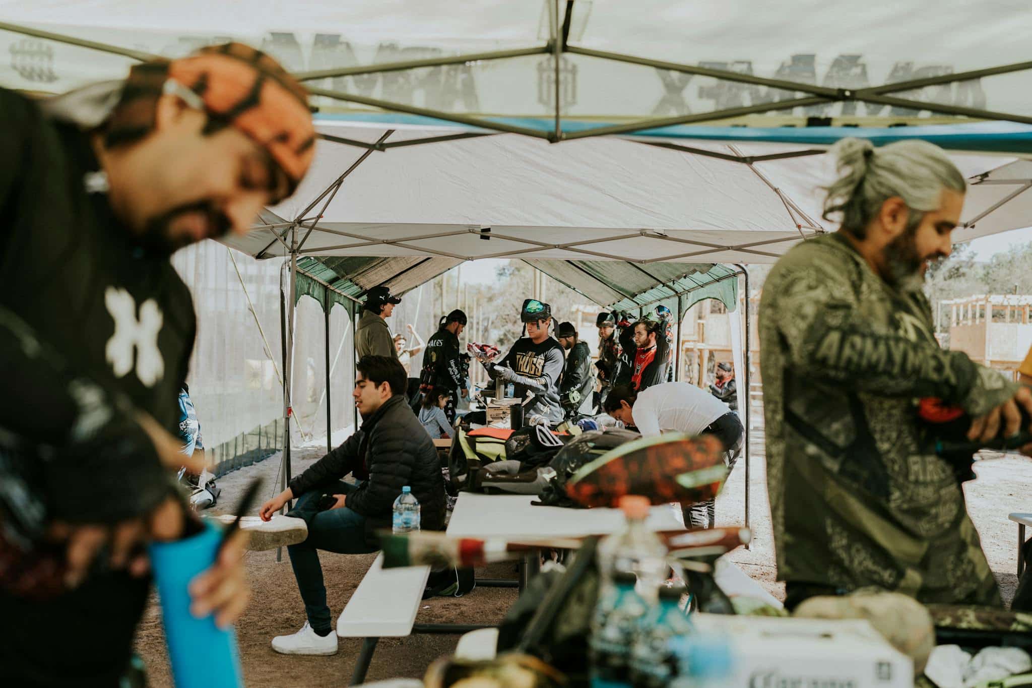 Paintball enthusiasts in protective gear preparing for an exciting match under a large canopy.