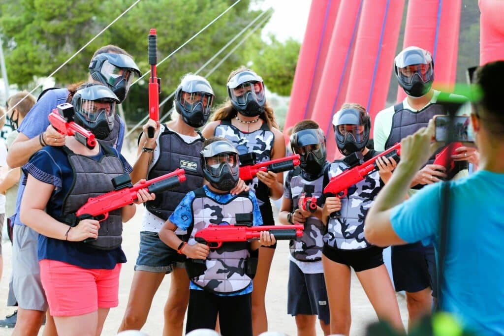 A group of people in protective gear posing for a photo during a paintball game outdoors.