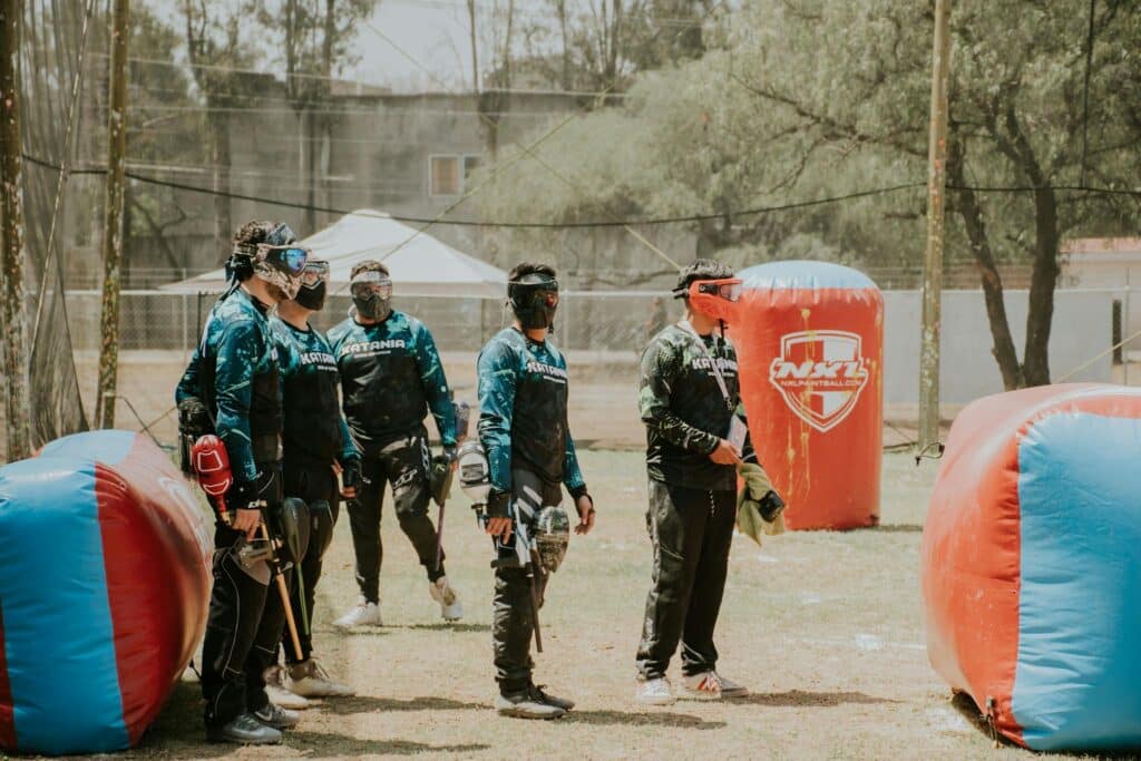 Un groupe de joueurs de paintball à Amiens en train d'élaborer une stratégie dans un terrain en plein air, équipés de leur matériel et de leurs masques.