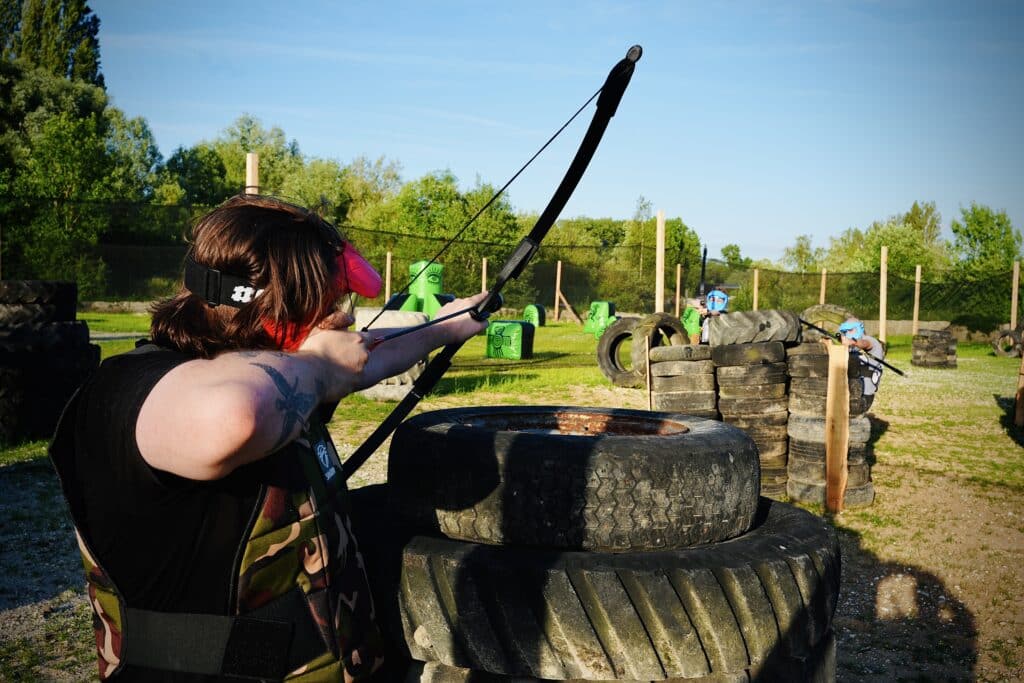 Joueur d'Archery Tag visant ses adversaires derrière une barricade de pneus à Amiens Paintball